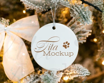 Könnte beinhalten: Weißer Keramik-Weihnachtsbaumschmuck mit einem braunen Pfotenabdruck und dem Text "tita mockup", der an einem schneebedeckten Weihnachtsbaum hängt.