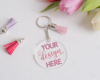 Op de afbeelding: Een transparante acryl sleutelhanger met een zilveren sleutelring en ketting. De sleutelhanger heeft een roze kwast en een roze inscriptie met de tekst "YOUR design HERE".