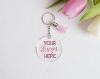 Op de afbeelding: Een transparante acryl sleutelhanger met een zilveren sleutelring en een roze kwast. De sleutelhanger heeft de tekst "YOUR design HERE" in roze gedrukt.