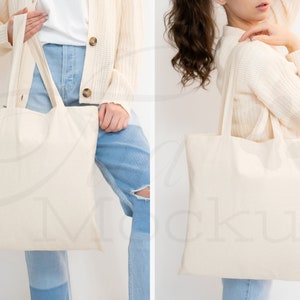 May include: Two people are holding a blank, off-white canvas tote bag. The bag has two long straps. The person on the left is wearing a white shirt, blue jeans, and a cream cardigan. The person on the right is wearing a cream sweater and blue jeans.