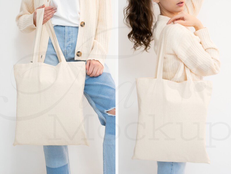 May include: Two people are holding a blank, off-white canvas tote bag. The bag has two long straps. The person on the left is wearing a white shirt, blue jeans, and a cream cardigan. The person on the right is wearing a cream sweater and blue jeans.