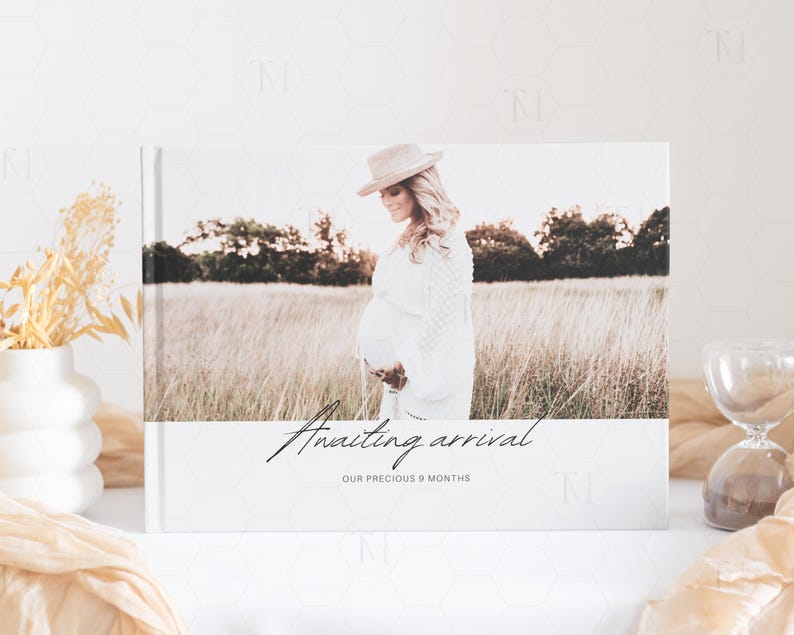 May include: A white photo album with a photo of a pregnant woman in a field. The text on the album reads "Awaiting arrival our precious 9 months".