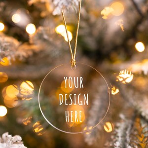 Peut inclure: Une boule de Noël ronde transparente avec un cordon doré suspendu à un sapin de Noël. La boule est ornée de l'inscription "YOUR DESIGN HERE".