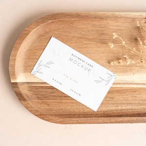 May include: A white business card mockup with a simple floral design and the text "Business Card Mockup" and "PSD & JPG 3.5 x 2 IN". The card is on a wooden tray with dried flowers.