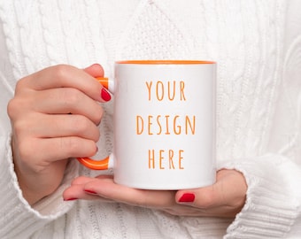 May include: White ceramic mug with an orange rim and handle. The mug has the text "YOUR DESIGN HERE" printed on the front.