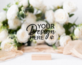 Peut inclure: Une pancarte en acrylique transparente avec une base en bois, comportant le texte "Your Design Here" et une empreinte de patte. La pancarte est posée sur une surface blanche avec un bouquet de roses blanches en arrière-plan.