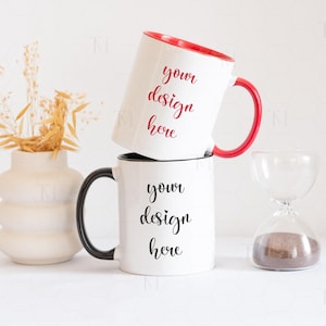May include: Two white ceramic mugs with black handles. The top mug has a red rim and the text "your design here" in red. The bottom mug has the text "your design here" in black.