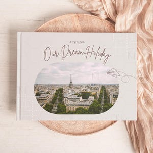 May include: A white photo album with a gray background and a photo of the Eiffel Tower in Paris. The album has the text "A Trip to Paris. Our Dream Holiday" on the front.