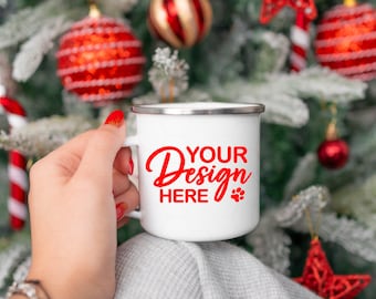 May include: White enamel mug with a red rim and handle. The mug has the text "YOUR Design HERE" in red lettering. The mug is being held by a hand in front of a Christmas tree decorated with red and white ornaments.