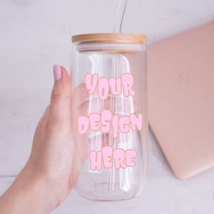 Puede incluir: Un vaso de vidrio transparente con tapa de bambú y una pajita rosa. El vaso tiene el texto "YOUR DESIGN HERE" impreso en rosa.