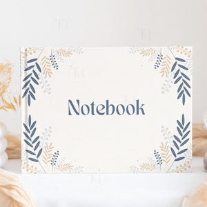 May include: A white notebook with a floral design in shades of blue and beige. The word "Notebook" is printed in the center of the cover.