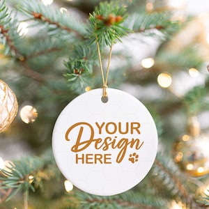 May include: White round ceramic bauble with gold string hanging on a Christmas tree. The bauble has the text "YOUR Design HERE" in gold lettering with a paw print.