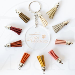 May include: A clear acrylic keychain mockup with a paw print and the text "Tila Mockup".  Surrounding the keychain are nine different coloured tassels with silver metal tops.
