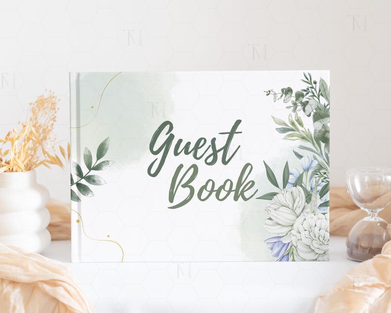 May include: A white guest book with a green watercolor background and floral illustrations. The text "Guest Book" is written in black cursive font.