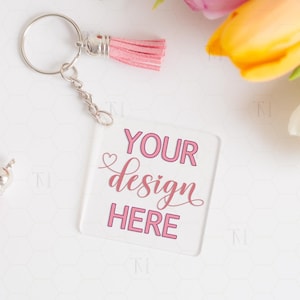 May include: A clear acrylic keychain with a silver key ring and a pink tassel. The keychain has the text "YOUR design HERE" printed on it in pink.