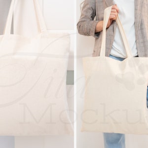 May include: Two white canvas tote bags. One bag is hanging on a hook and the other is being held by a person wearing a gray blazer and blue jeans.