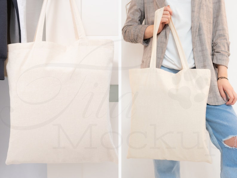May include: Two white canvas tote bags. One bag is hanging on a hook and the other is being held by a person wearing a gray blazer and blue jeans.