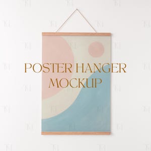 May include: A poster mockup with a wooden frame and a hanging string. The poster features an abstract design with soft pastel colors, including pink, blue, and cream. The text "POSTER HANGER MOCKUP" is displayed in a gold color.