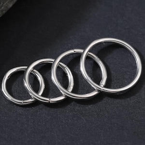 Könnte beinhalten: Ein Set aus vier kreisförmigen, silberfarbenen Metallringen, die in einer Reihe von klein nach groß angeordnet sind. Jeder Ring verfügt über eine glatte, polierte Oberfläche und ein nahtloses, durchgehendes Banddesign.
