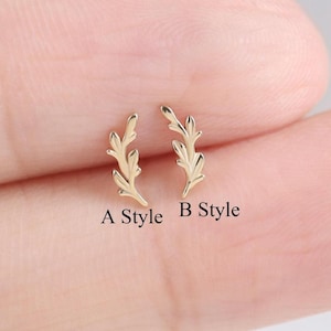 May include: Two gold-colored leaf-shaped stud earrings. The earrings are displayed on a light background. The text "A Style" and "B Style" are below each earring. The earrings are small and delicate.