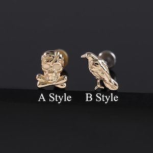 May include: Two gold-colored stud earrings. One earring features a skull and crossbones design, labeled "A Style." The other earring is a raven, labeled "B Style." The earrings are displayed on a dark surface.