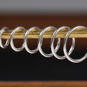 Peut inclure: Un ensemble de six anneaux circulaires de couleur argentée avec des diamètres variés, chacun présentant une finition lisse et polie. Les anneaux sont disposés en rangée, suspendus sur une fine tige métallique horizontale dorée.