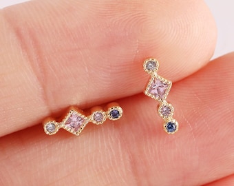 May include: A pair of gold earrings with small, colorful gemstones. One earring has a straight design with four gemstones, while the other has a curved design with five gemstones.