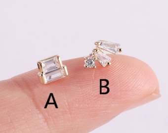 May include: Two different styles of earrings with clear cubic zirconia stones. The first earring is a single square stone. The second earring has a cluster of three stones, one round and two baguette shaped.