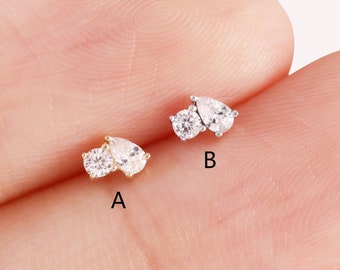 Puede incluir: Dos pares de pendientes con piedras transparentes en forma de pera. Los pendientes se muestran en una mano, con el pendiente izquierdo en oro y el derecho en plata. Los pendientes están etiquetados como A y B.