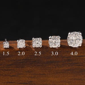 Puede incluir: Una colección de cinco pendientes de diamantes de diferentes tamaños, que van de 1,5 a 4,0, expuestos sobre una superficie de madera. Los pendientes están engastados en plata u oro blanco, con el tamaño en quilates claramente etiquetado.