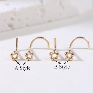 May include: Two gold-colored nose rings, each with a small, five-petal flower design. One ring is labeled "A Style" and the other is labeled "B Style". The flower petals are made of small, round beads. The background is a white, textured surface.