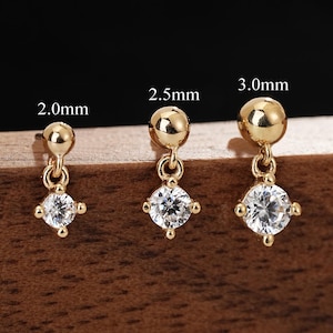Puede incluir: Tres pendientes colgantes de oro con una cuenta redonda en la parte superior y una piedra transparente facetada. Los pendientes están etiquetados con los tamaños 2,0 mm, 2,5 mm y 3,0 mm, indicando el diámetro de la cuenta superior.