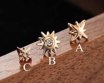 Puede incluir: Tres pendientes de botón dorados etiquetados como A, B y C. El pendiente A es una estrella de cuatro puntas, el B tiene forma de sol con una piedra clara central y el C es una estrella más pequeña con una pequeña piedra clara central.