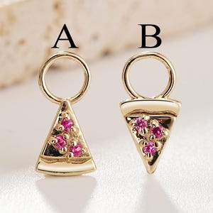 May include: Two gold jewelry charms labeled A and B. Charm A is a triangular slice shape with three small pink stones. Charm B is a wider triangular slice shape with three small pink stones. Both charms feature a circular loop at the top for attachment.
