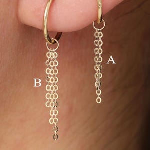 May include: A close-up of two gold hoop earrings. One earring features a delicate chain of small links, while the other has a longer, cascading chain design. The earrings are displayed on an ear, showcasing their elegant and minimalist style.