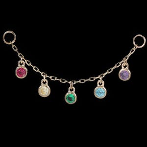 Può includere: Una delicata catena d'oro con sei ciondoli di pietre preziose colorate. I ciondoli sono rotondi e presentano una varietà di colori, tra cui rosso, giallo, verde, blu e viola. La catena ha due piccoli anelli a ciascuna estremità.