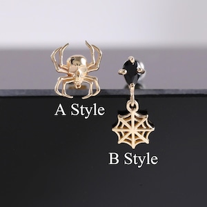 May include: Two gold-colored earrings. One is a spider, and the other features a black gem and a spiderweb design. The text "A Style" and "B Style" are printed below each earring. The earrings are displayed on a black surface.