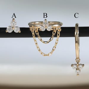 以下が含まれることがあります： A、B、Cとラベル付けされた3つのゴールドジュエリー。Aは3石のスタッドピアス。Bは3石のクラスターと2本のドレープチェーンが付いたゴールドリング。Cは3石のクラスターチャームがぶら下がったゴールドのフープピアス。