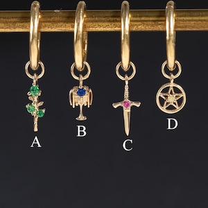 May include: Four gold hoop earrings with dangling charms labelled A, B, C, and D. Charm A is a green stone branch, B is a chalice with a blue stone, C is a sword with a pink stone, and D is a circular star emblem. Each charm hangs from a gold hoop.
