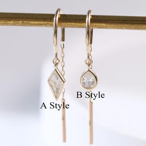 May include: Two pairs of gold-colored earrings. One pair features a diamond-shaped clear stone, the other a teardrop-shaped clear stone. Both pairs have a dangling bar and are labeled "A Style" and "B Style".