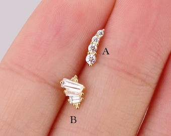 May include: Two gold earrings with clear cubic zirconia stones. The earring on the left is a cluster of small stones in a geometric shape. The earring on the right is a row of five stones in a curved shape. The earrings are labeled A and B.
