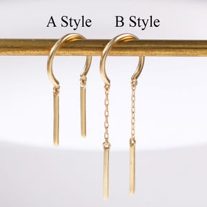 May include: Two pairs of gold-coloured earrings are displayed. One pair features a simple bar pendant, while the other has a chain with a bar pendant. The text "A Style" and "B Style" are above the earrings.