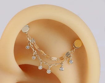 May include: Gold chain ear cuff with dangling clear gemstones. The chain is made of two strands with oval links. The ear cuff is designed to be worn on the upper cartilage of the ear.