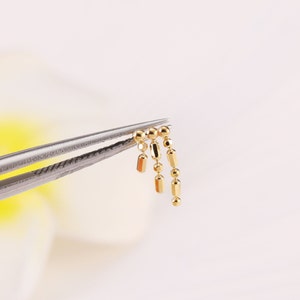May include: A gold chain with round and rectangular links. The chain is held by a pair of tweezers.