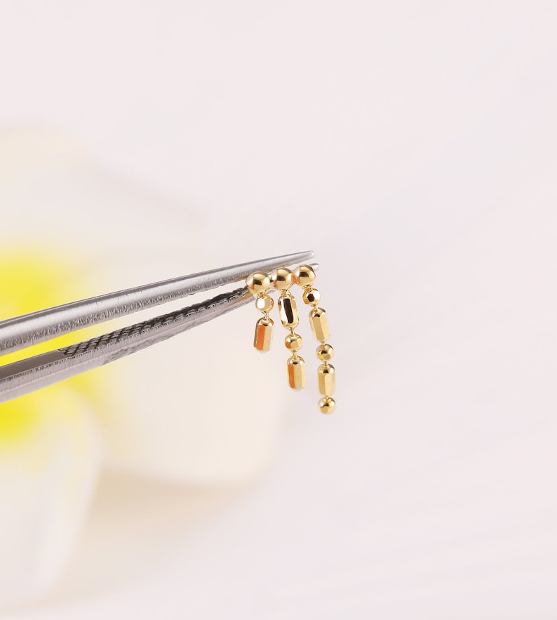 May include: A gold chain with round and rectangular links. The chain is held by a pair of tweezers.
