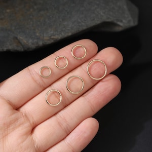 May include: A collection of six gold-toned circular rings of varying sizes arranged in a cluster. Each ring features a smooth, thin, continuous metal band with a simple, circular design, showcasing a polished finish that reflects light.