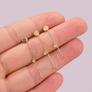 May include: Three gold dangle earrings with a small round disc at the top and a small clear stone at the bottom of each chain.