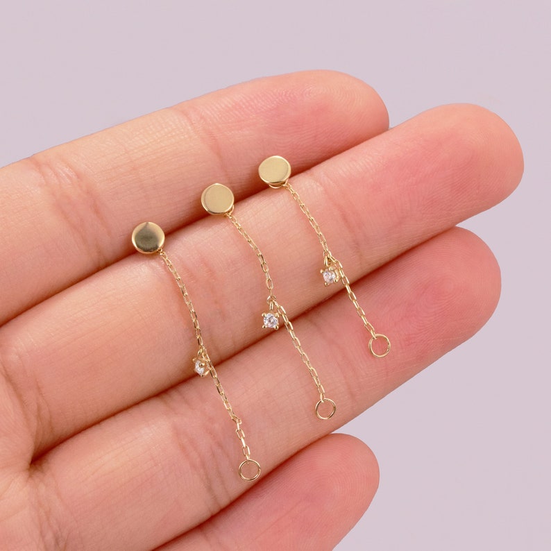 May include: Three gold dangle earrings with a small round disc at the top and a small clear stone at the bottom of each chain.