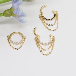 May include: Three gold hoop earrings with dangling chains. The hoops are adorned with clear cubic zirconia stones. The chains are made of gold and have a delicate, chain-link design.