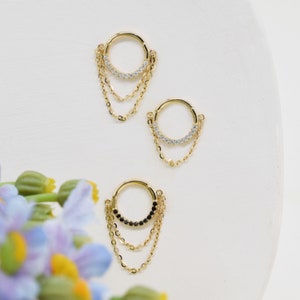 May include: Two gold hoop earrings with dangling chains. One hoop is adorned with clear cubic zirconia stones, the other with black cubic zirconia stones.